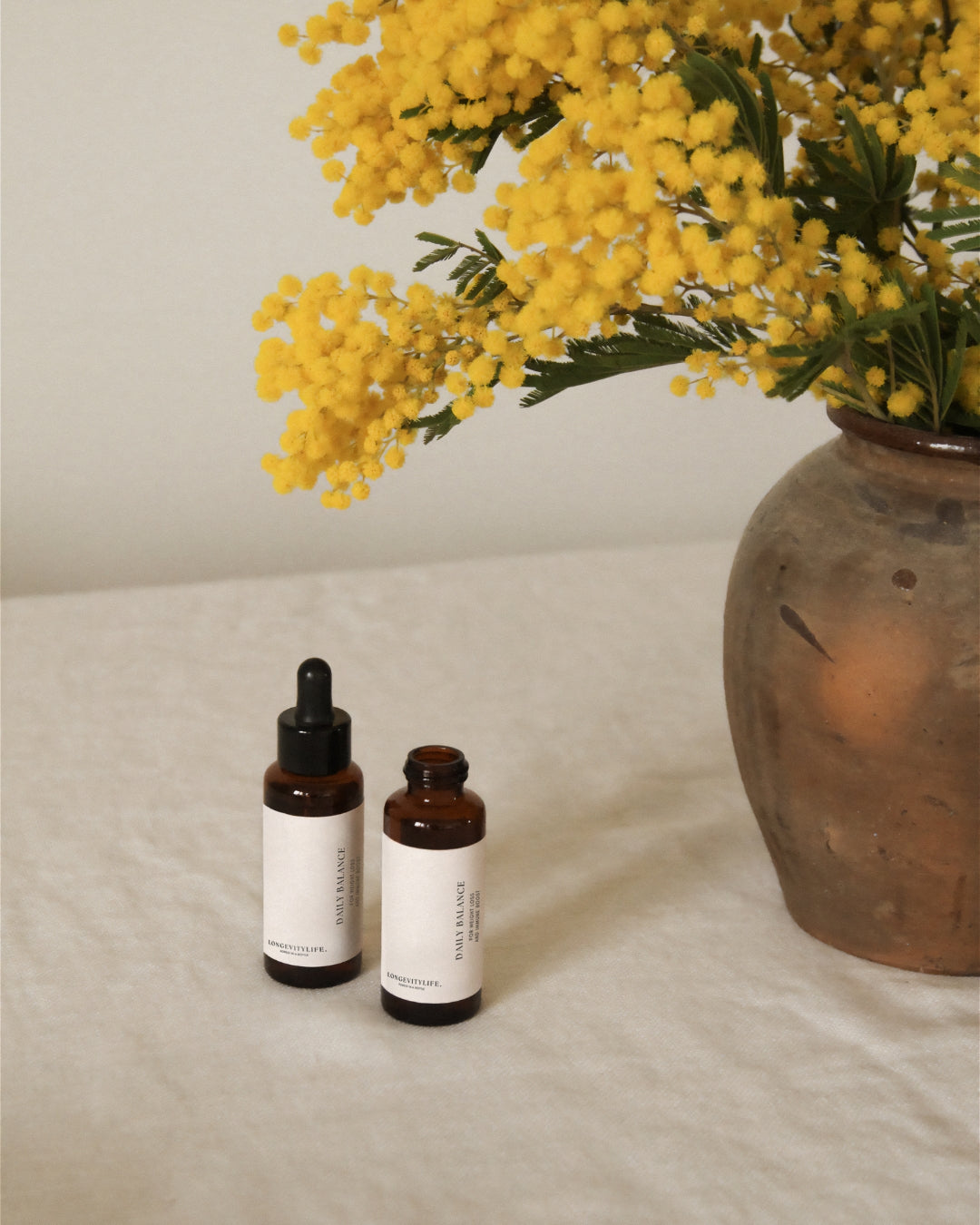 A decorative vase with bright yellow flowers and two small bottles of Daily Balance oils placed on a table.