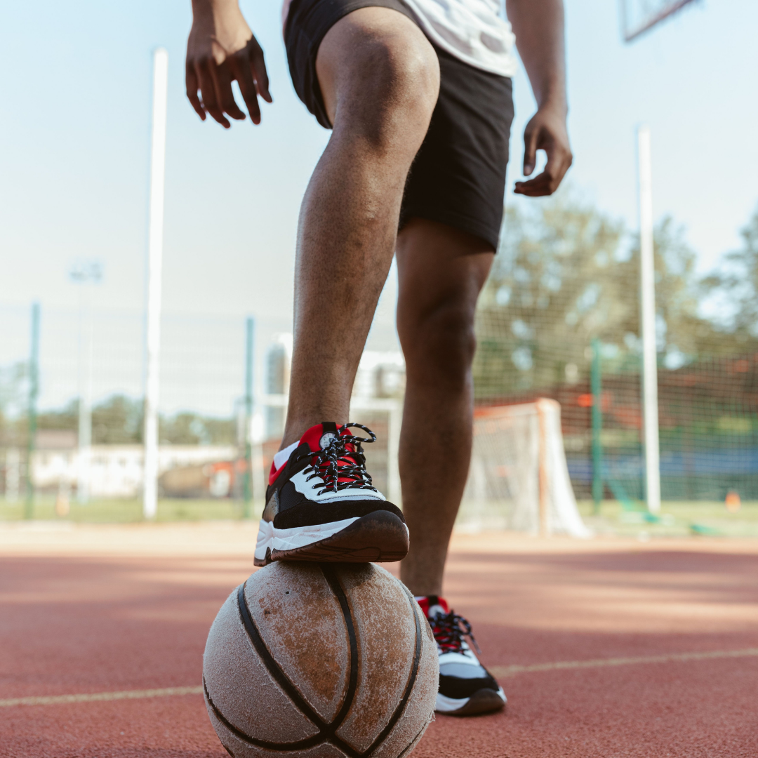 Sportler stellt den Fuß auf einen Basketball auf einem roten Sportplatz, Thema Nasenstrips und Schlaf im Sport
