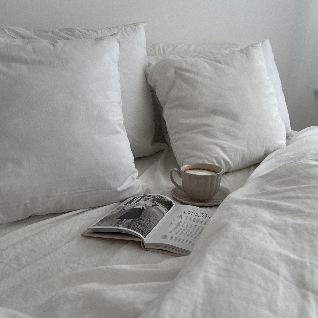 Aufgeschlagenes Magazin und Tasse Kaffee auf weißer Bettwäsche, Sinnbild für eine ruhige Abendroutine vor dem Schlafen