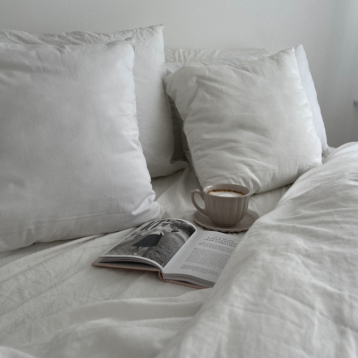 Aufgeschlagenes Magazin und Tasse Kaffee auf weißer Bettwäsche, Sinnbild für eine ruhige Abendroutine vor dem Schlafen