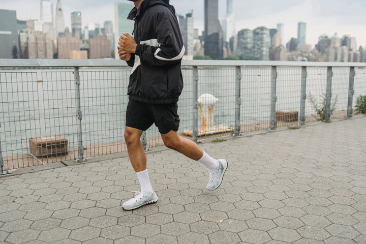 Mann in schwarzer Jacke joggt an einer Uferpromenade vor der Skyline, Fitness als Gewohnheit für ein längeres Leben