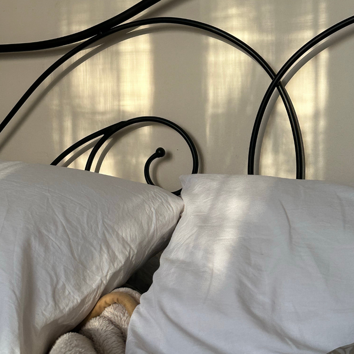 Zerwühltes weißes Bettzeug vor schwarzem Metallbett im Morgenlicht, Sinnbild für Mundatmung in der Nacht