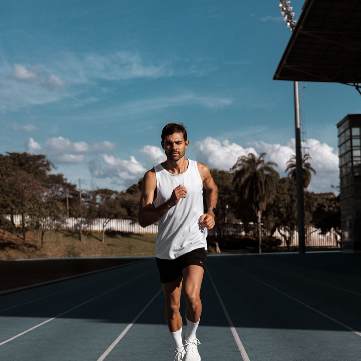 Mann im weißen Tanktop läuft auf einer blauen Laufbahn im Stadion, Thema Nasenstrips beim Training