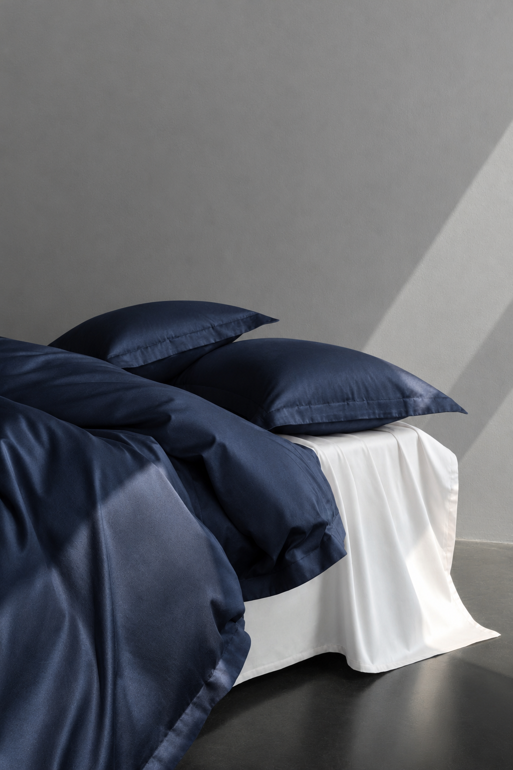 Bett mit dunkelblauer Bettwäsche im Morgenlicht