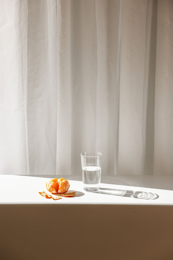 Geschälte Mandarine und ein Glas Wasser im Morgenlicht, einfache Lebensmittel für ein langes Leben