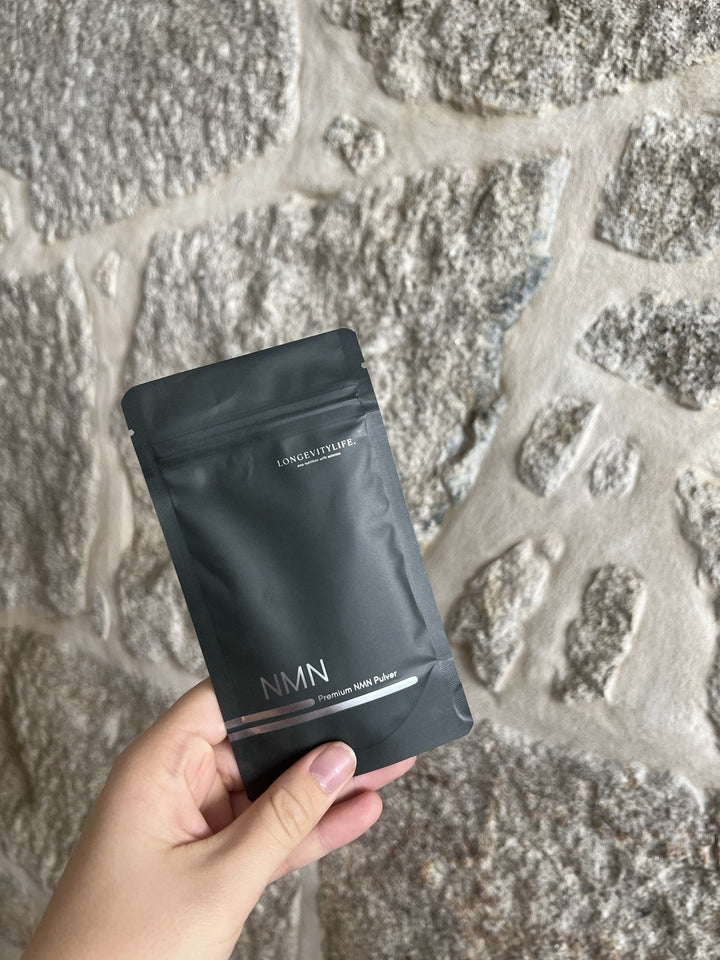 NMN Beutel von LongevityLife in der Hand vor heller Steinmauer