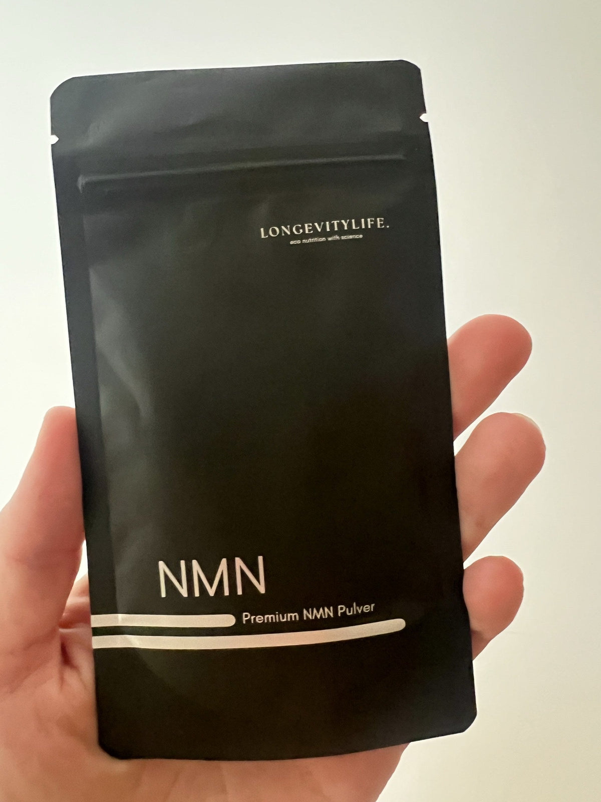 Hand hält den schwarzen Beutel Premium NMN Pulver von LongevityLife