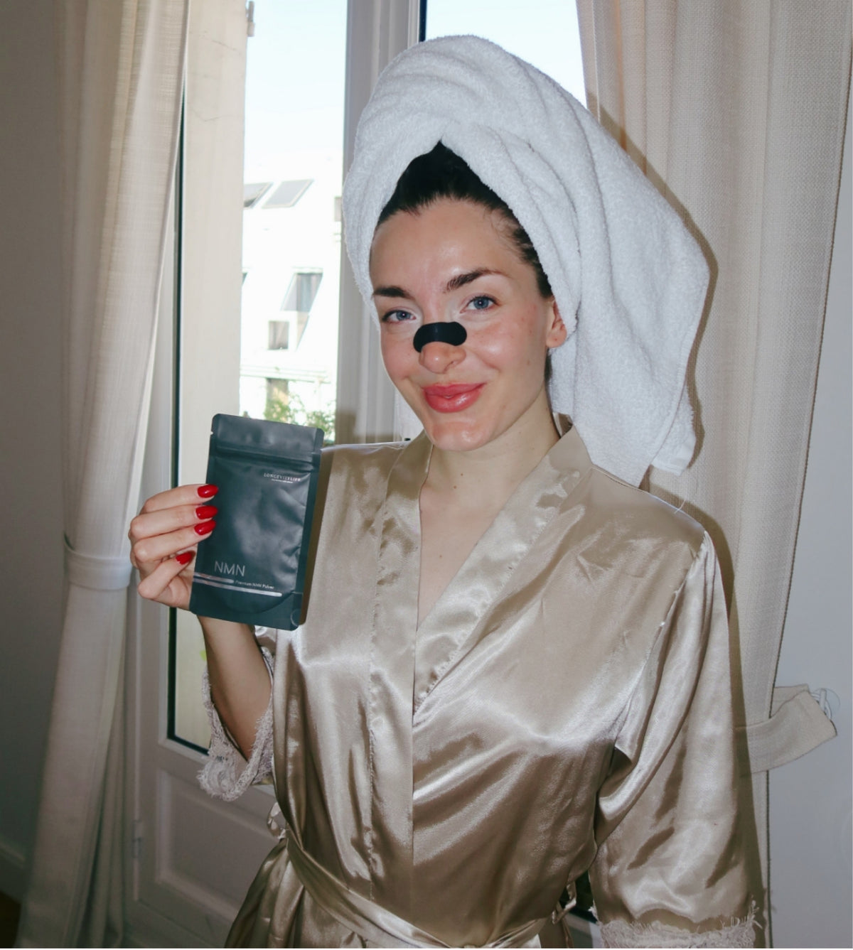 Miriam Janke mit Handtuch, Nasenstrip und NMN Beutel am Fenster