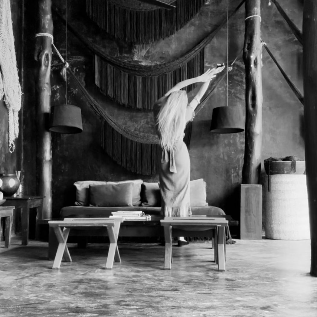 In a softly lit room, a woman stands beside a hammock, creating a relaxed and inviting atmosphere.
