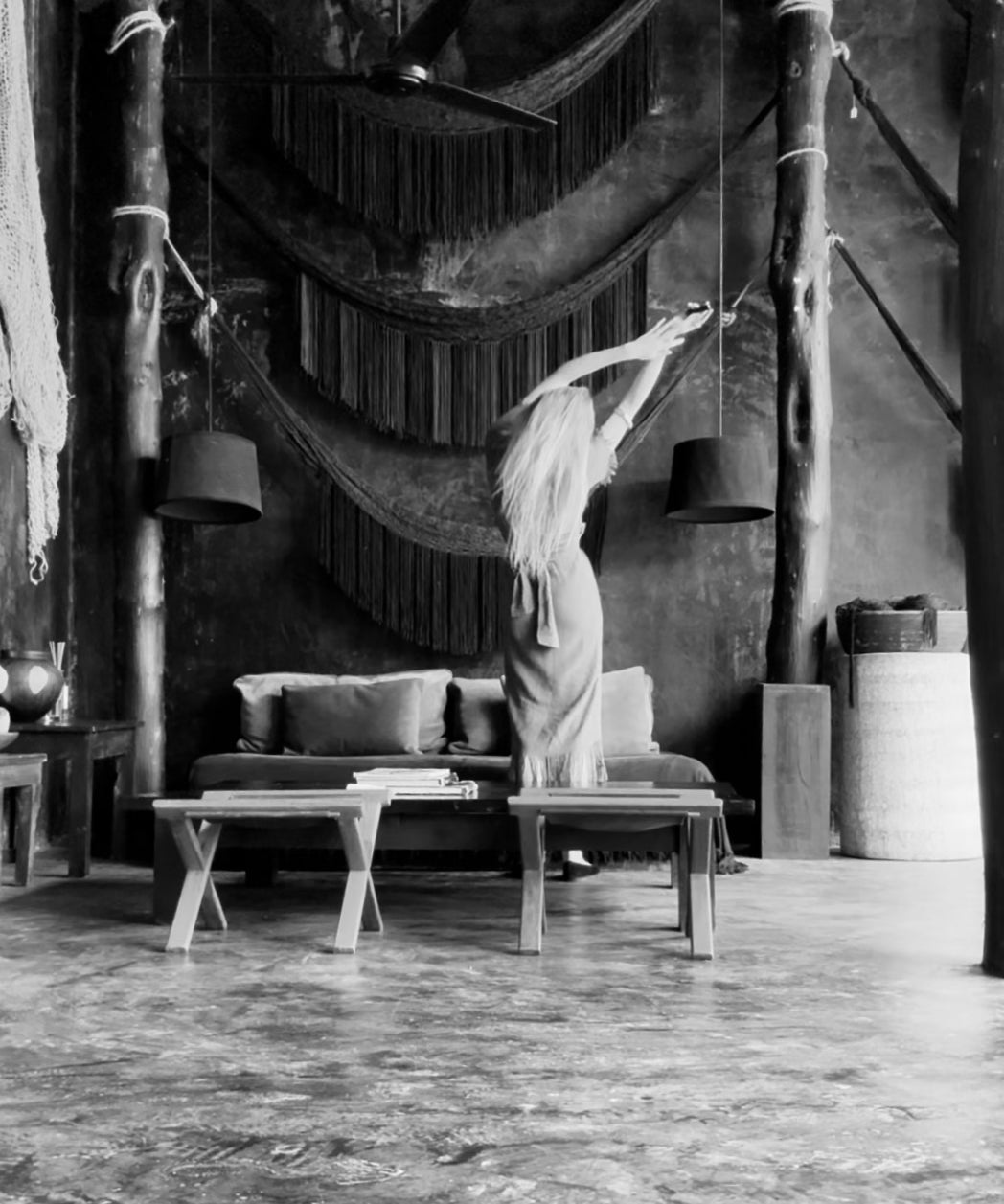 In a softly lit room, a woman stands beside a hammock, creating a relaxed and inviting atmosphere.