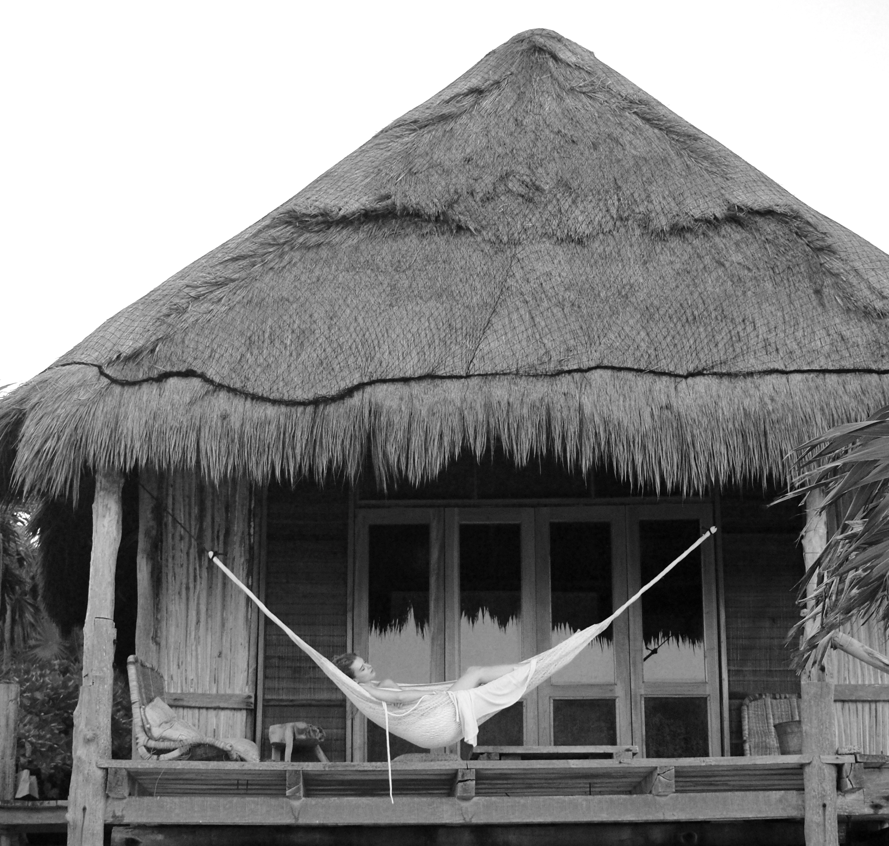  woman relaxes in a hammock on the porch of a rustic hut, surrounded by greenery and sunlight.