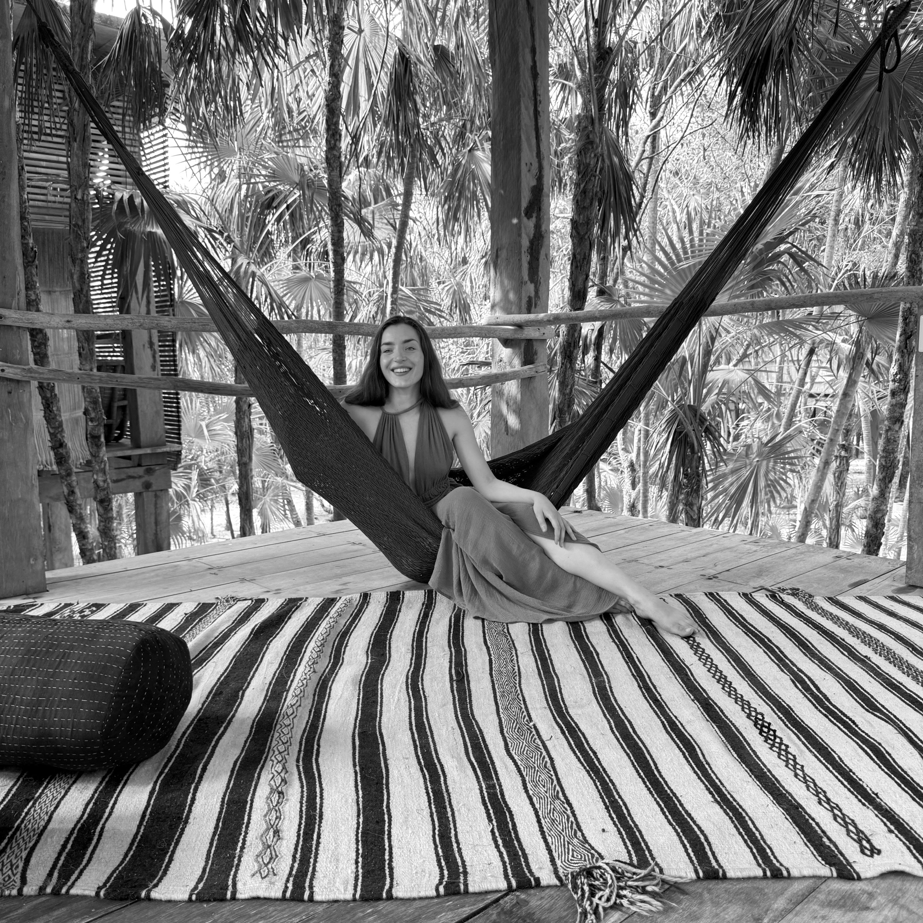 A woman reclines in a hammock, resting on a patterned rug, enjoying a moment of leisure.