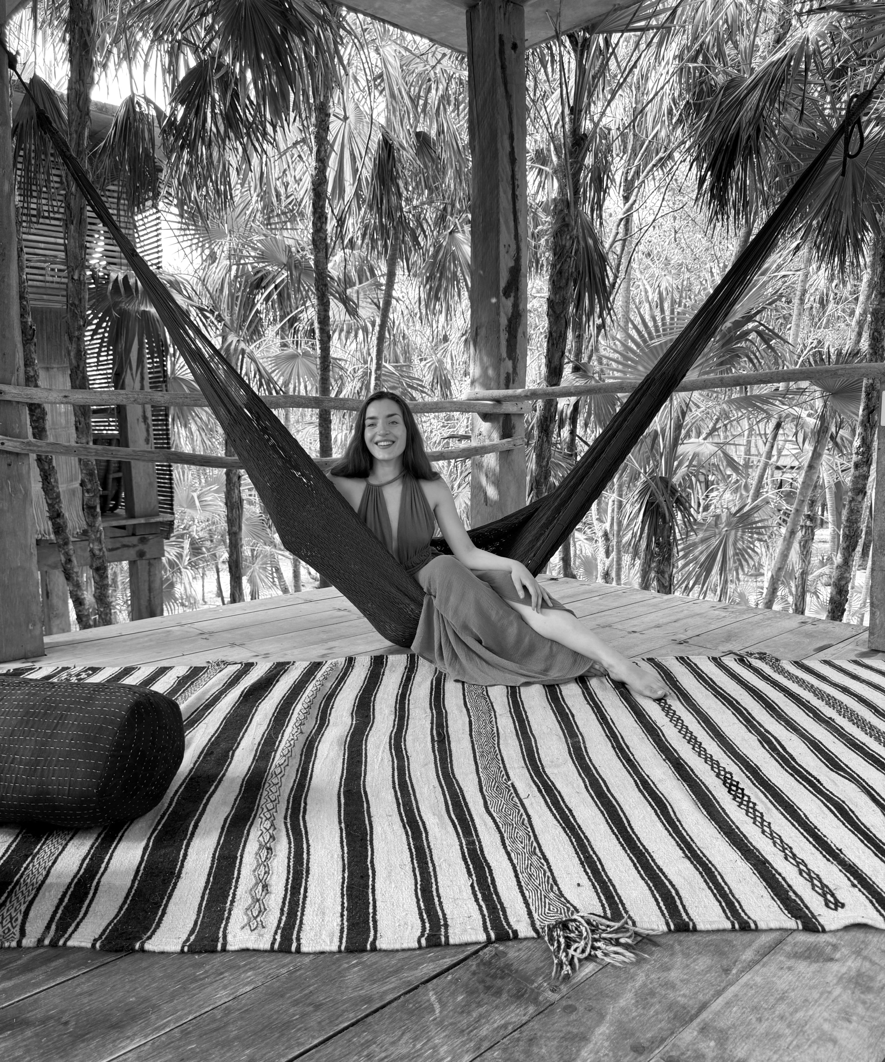 A woman reclines in a hammock, resting on a patterned rug, enjoying a moment of leisure.