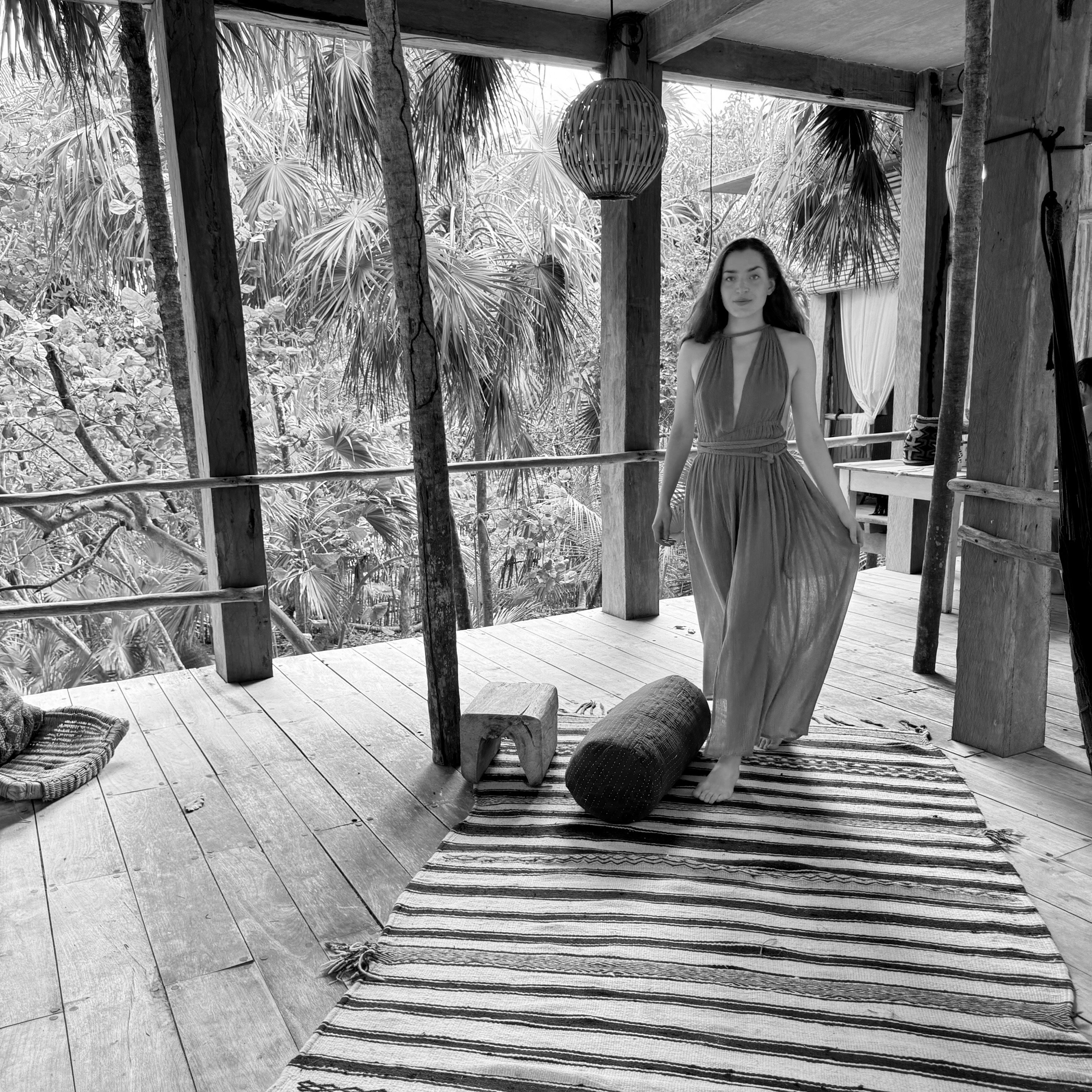 A woman stands on a rug in a cozy room, with a tree visible in the background, creating a warm atmosphere.