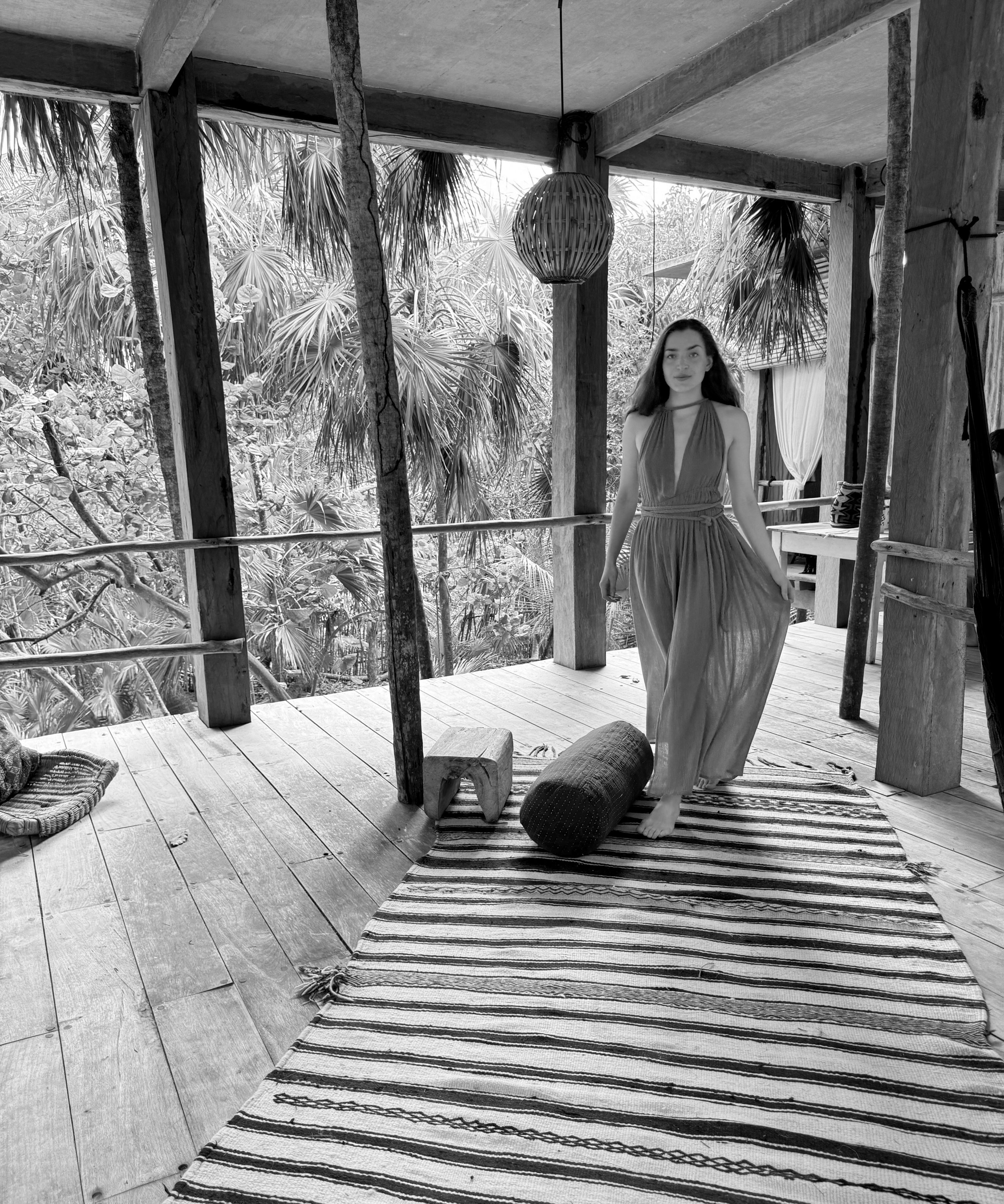 A woman stands on a rug in a cozy room, with a tree visible in the background, creating a warm atmosphere.