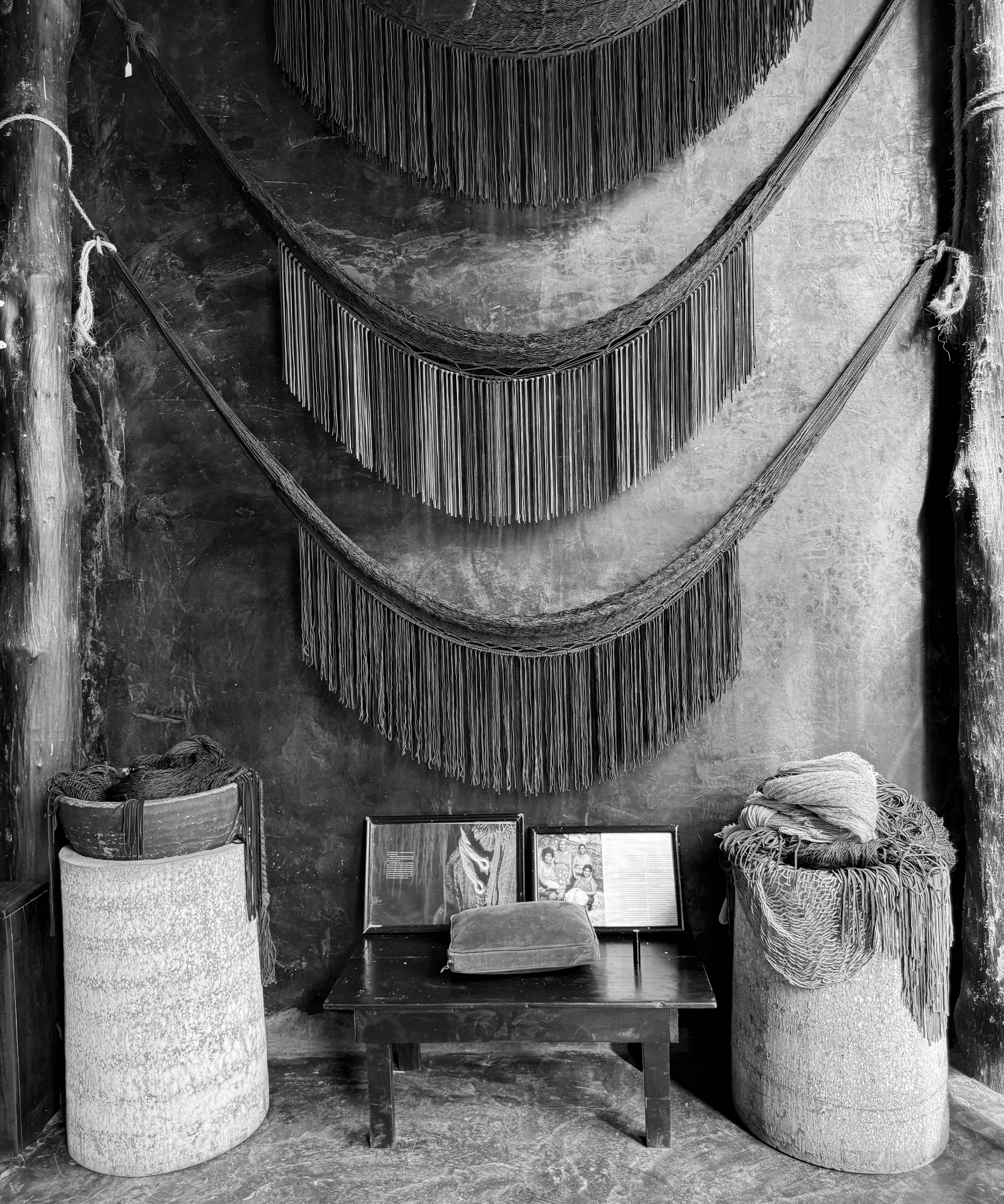 A black and white photo of a room featuring woven baskets and a wall adorned with decorative tassels.