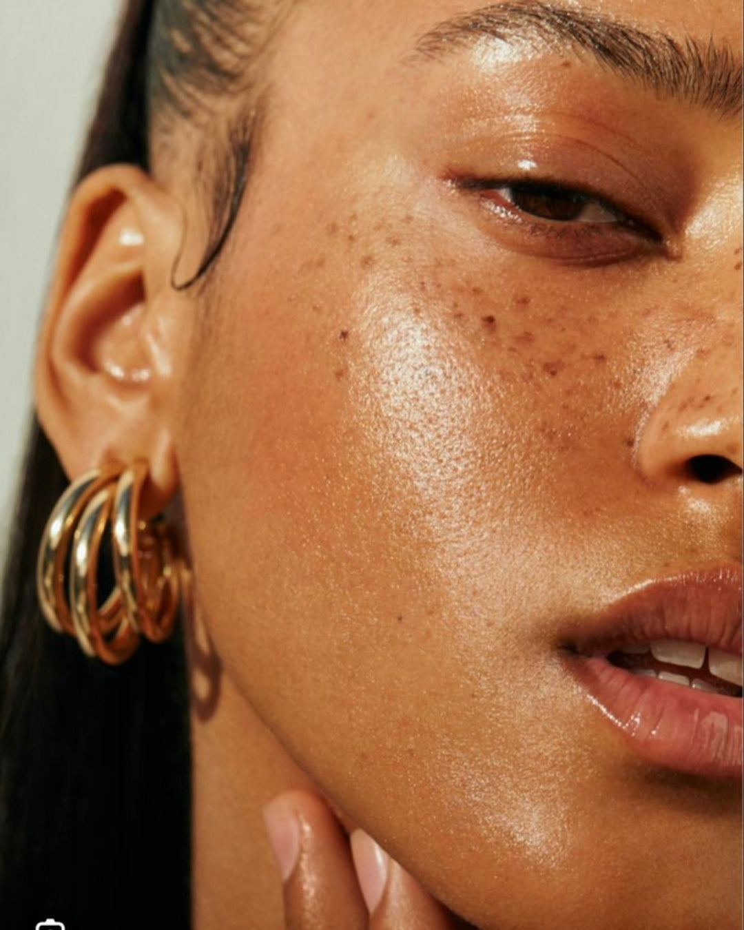 A woman with a freckled complexion wears gold hoop earrings, highlighting her facial features and personal style.