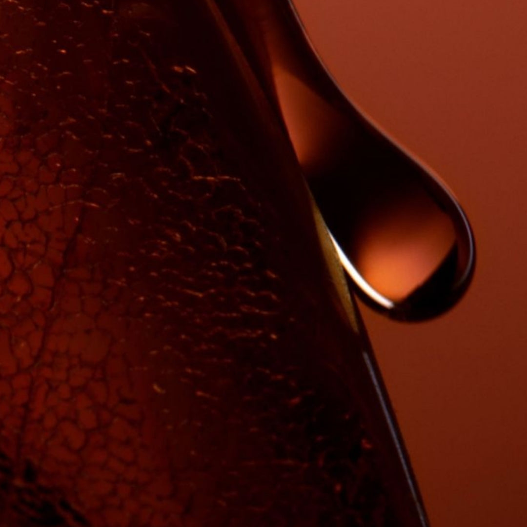 A close-up of a single drop of liquid glistening in the foreground against a blurred background.
