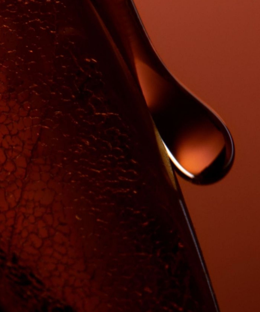 A close-up of a single drop of liquid glistening in the foreground against a blurred background.