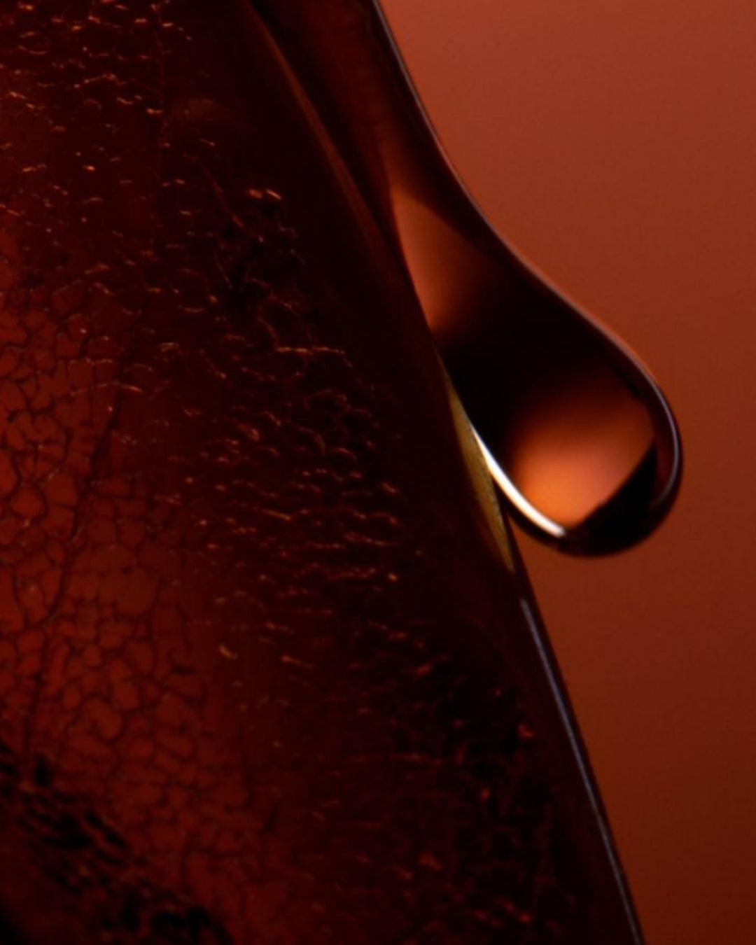 A close-up of a single drop of liquid glistening in the foreground against a blurred background.