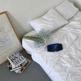 Silk-Schlafmaske in Dunkelblau auf einem Bett mit weißer Bettwäsche und Schleierkraut