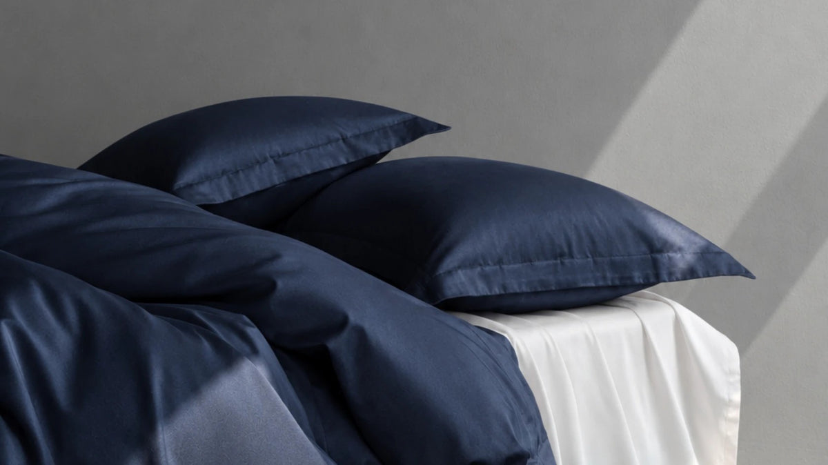 Silk-Kissenbezüge und Bettwäsche in Night Blue auf einem Bett mit weißem Laken im Tageslicht